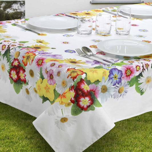 Tovaglia bianca in puro cotone su un tavolo apparecchiato all'aperto, decorata con una vivace bordatura di fiori colorati tra cui margherite, girasoli e primule.